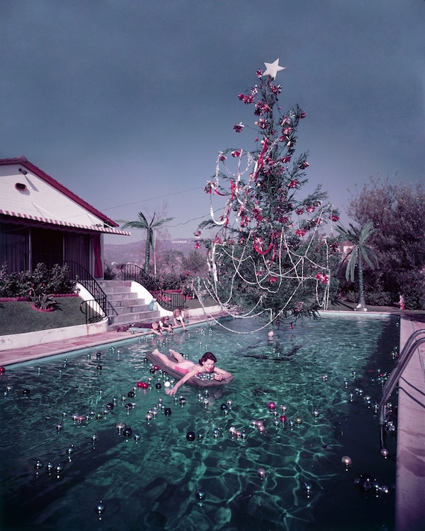 Rita Aarons, moglie del fotografo Slim Aarons, su un materassino in piscina con le decorazioni natalizie, in lontananza si può scorgere la scritta Hollywood 1954 (Photo by Slim Aarons/Hulton Archive/Getty Images)